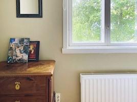 Una habitación con un aparador de madera, dos libros, un espejo y una ventana con vista a árboles.