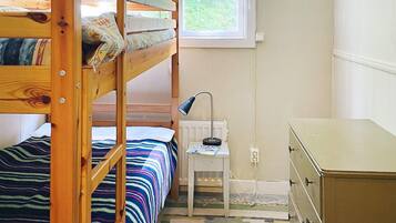 A bunk bed with a striped bedspread, a desk with a lamp, and a dresser in a room with a window.
