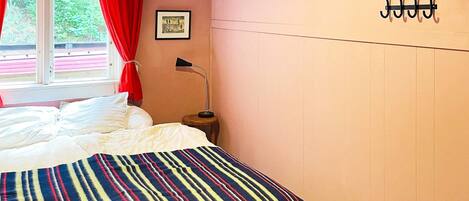 Un dormitorio con cama, cortinas en la ventana, una lámpara de noche y un perchero en la pared.