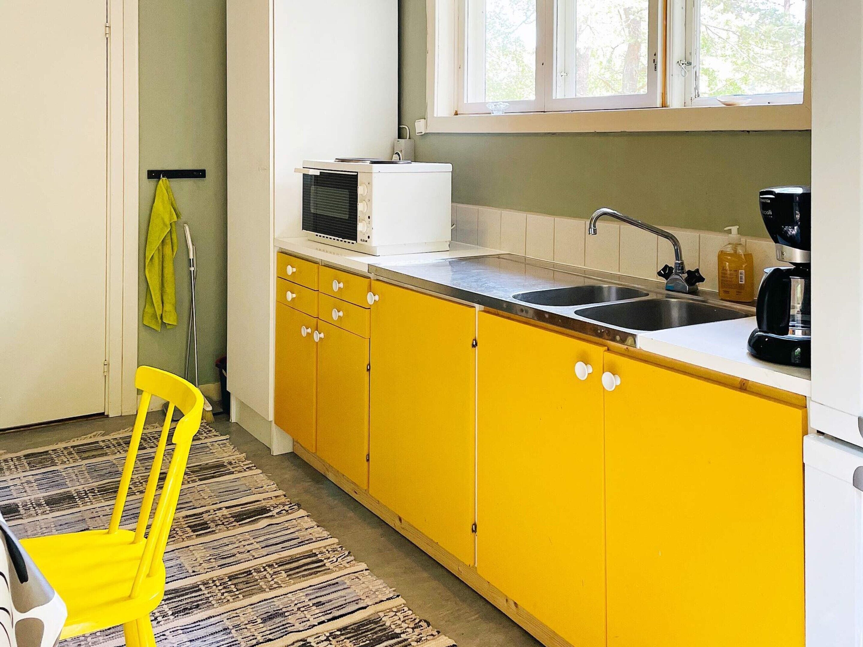 A kitchen with yellow cabinets, a white countertop, a sink, a microwave, and a coffee maker.