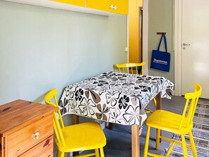 A room with a table covered by a patterned tablecloth, two yellow chairs, a wooden chest of drawers, and a blue bag hanging on the wall. - 6 Person Holiday Home in Henan (Henån)