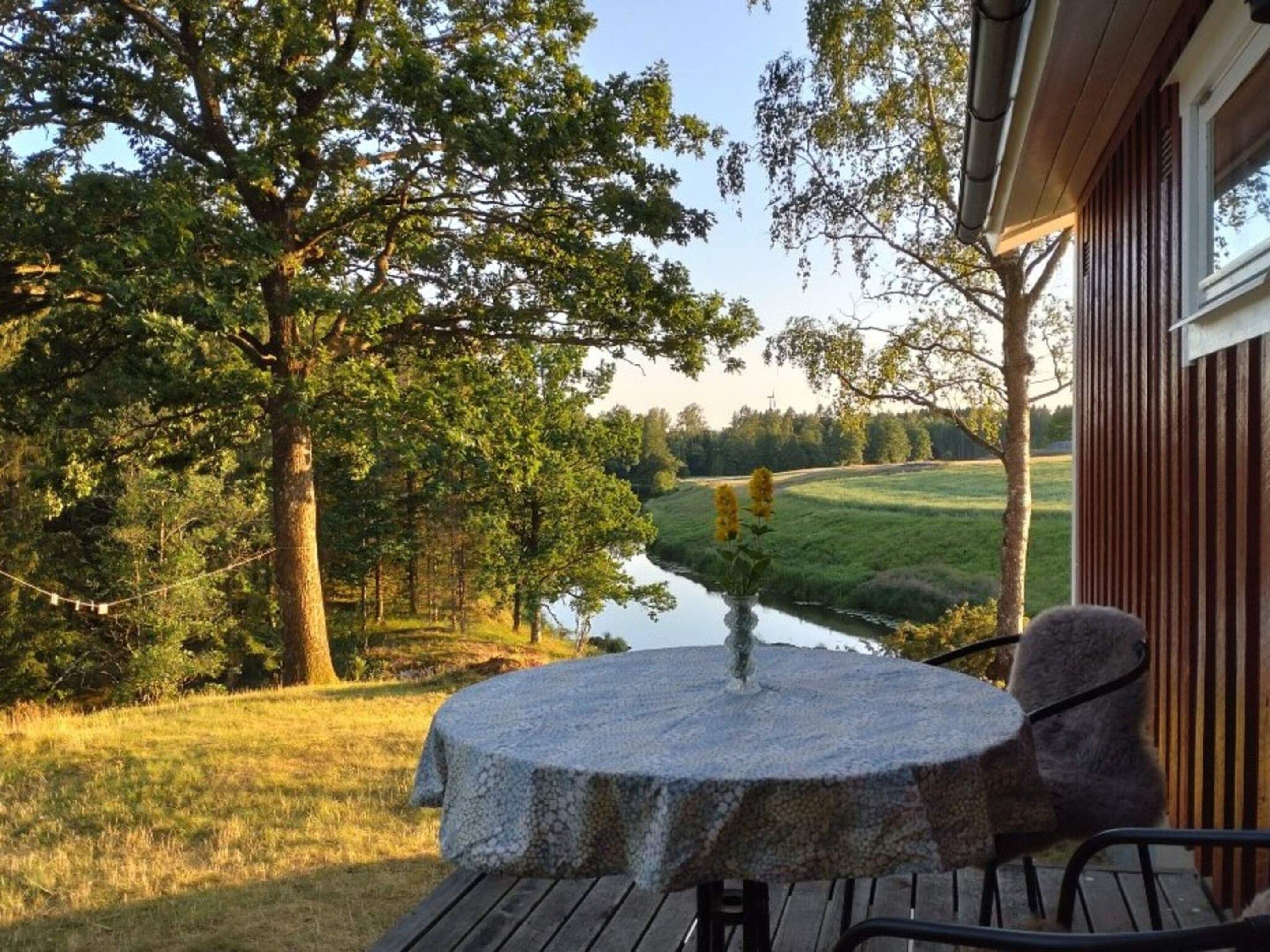 Una mesa de piedra con una silla frente a un edificio, con vistas a un río y follaje.