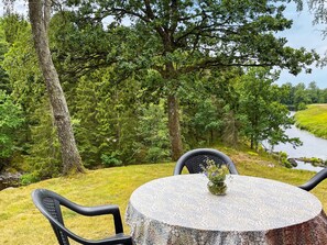 An outdoor seating area with a round table and chairs, overlooking a river and dense greenery. - 4 Star Holiday Home in Mellerud (Mellerud)