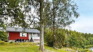 A red and white cabin with a porch, surrounded by a grassy area and trees. - 4 Star Holiday Home in Mellerud (Mellerud)