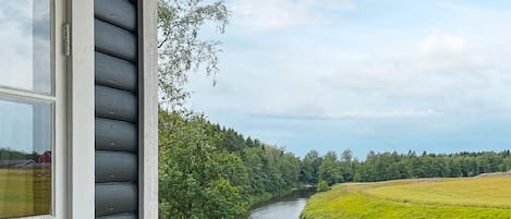 A river view from a porch with a railing, a window, and a view of a forested area.