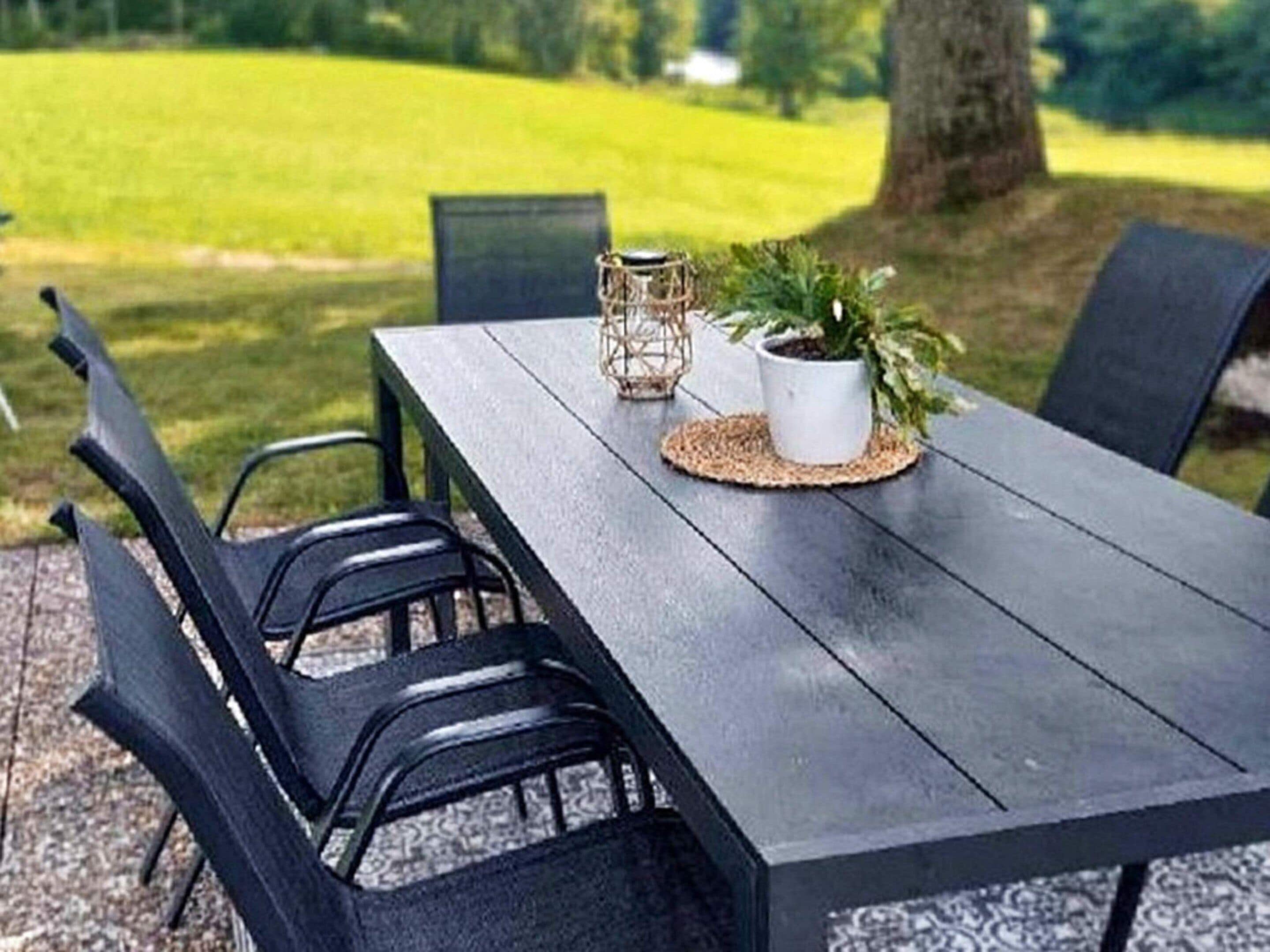 An outdoor dining area with a table, chairs, and a potted plant.