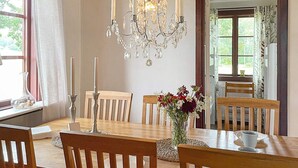 A dining room with a chandelier, wooden chairs, a table with a vase of flowers, and a window with curtains. - 4 Star Holiday Home in Mellerud (Mellerud)