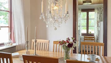A dining room with a chandelier, wooden chairs, a table with a vase of flowers, and a window with curtains.