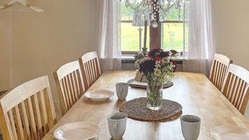 A dining room with a wooden table, chairs, a chandelier, and a window with curtains.