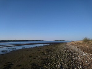 Uma praia com areia de pedrinhas e um céu azul límpido.