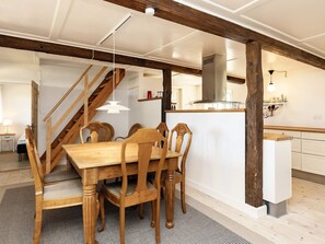 A dining area with a wooden table and chairs, a staircase, and a kitchen area with a white countertop. - 6 Person Holiday Home in Guldborg (Guldborg)