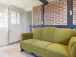 A room with a green sofa, a white door, and a brick wall. - 6 Person Holiday Home in Guldborg (Guldborg)