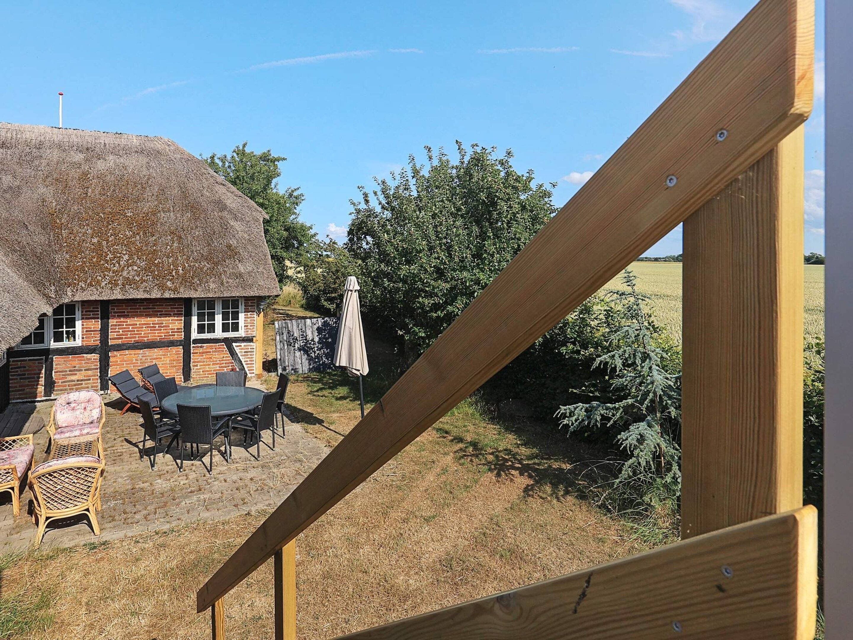 A thatched-roof house with a brick exterior, a dining table with chairs, and a wooden deck.
