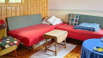 A cozy room with two beds, a wooden table, and a window with wooden paneled walls.