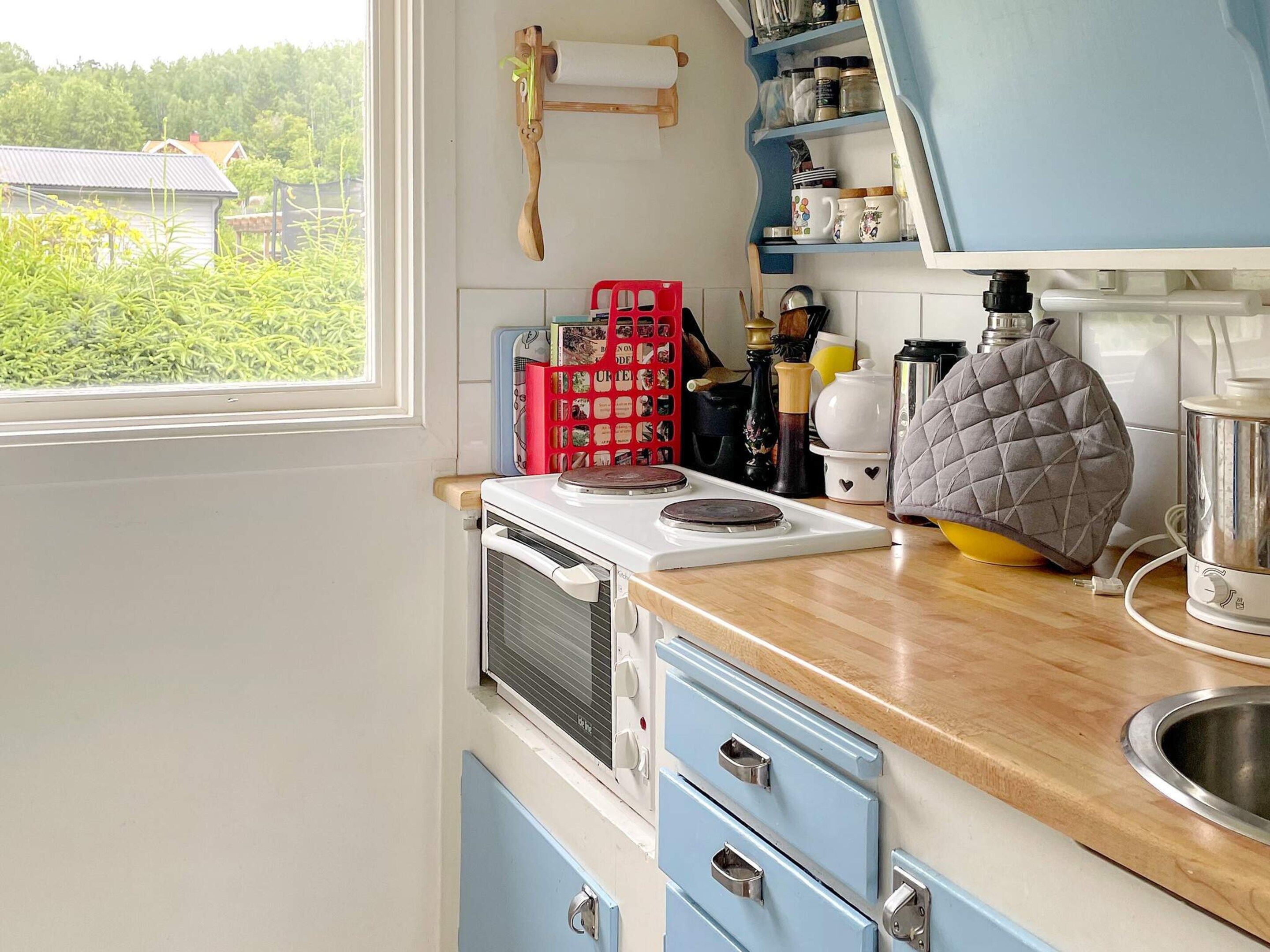 A kitchen with a stove, a sink, and a window overlooking greenery.