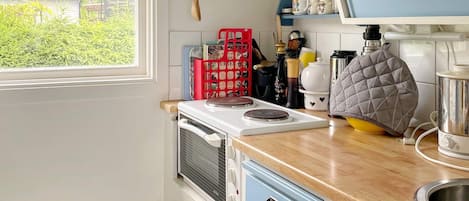 A kitchen with a stove, a sink, and a window overlooking greenery.