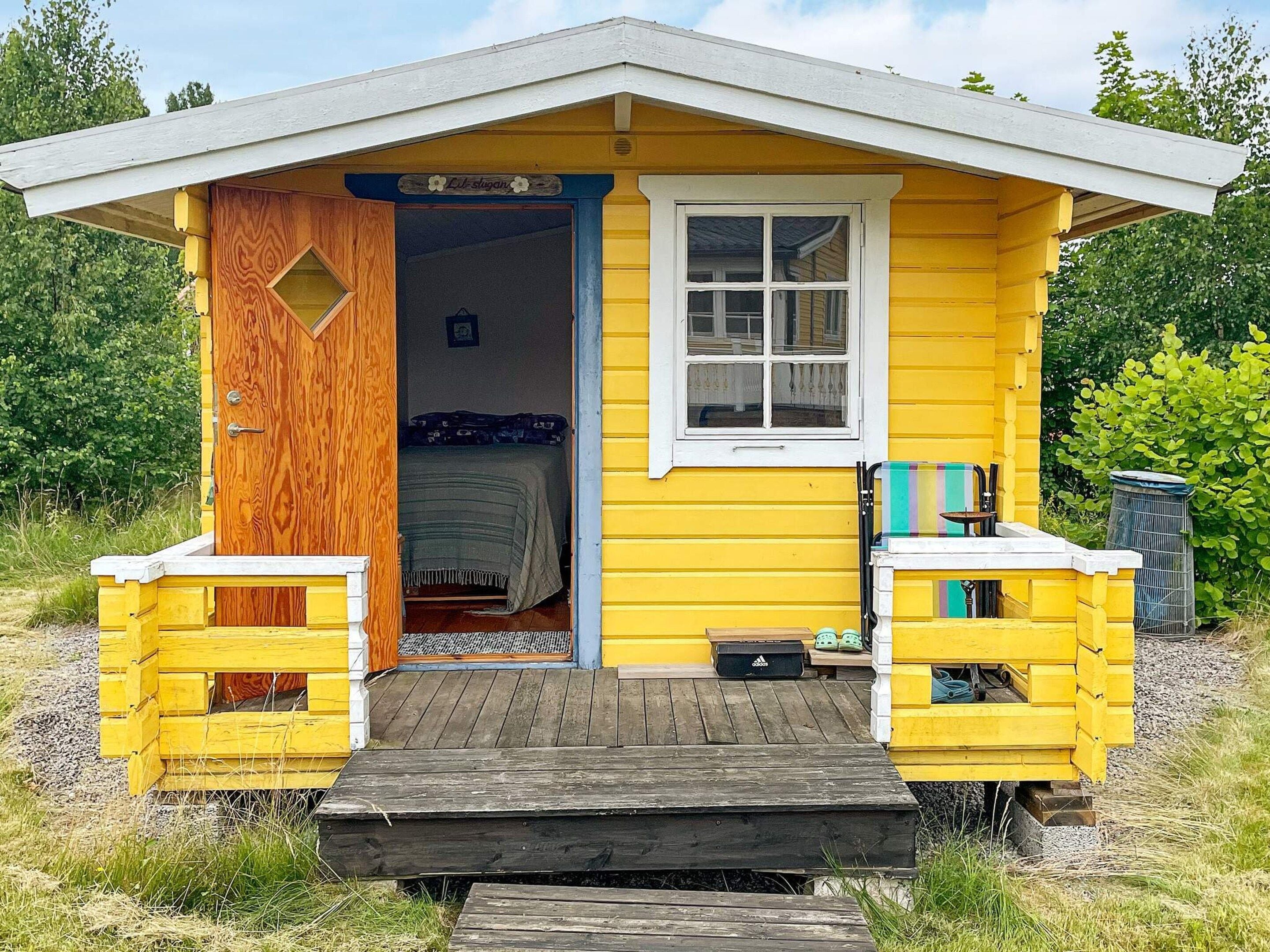 A small yellow cabin with a wooden door, a window, and a small porch area.