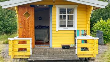A small yellow cabin with a wooden door, a window, and a small porch area.