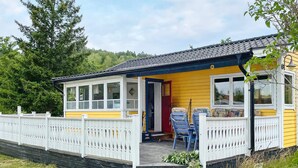 A yellow cottage with a white porch, two blue chairs, and a small table. - 4 Person Holiday Home in Kolmarden (Kolmården)
