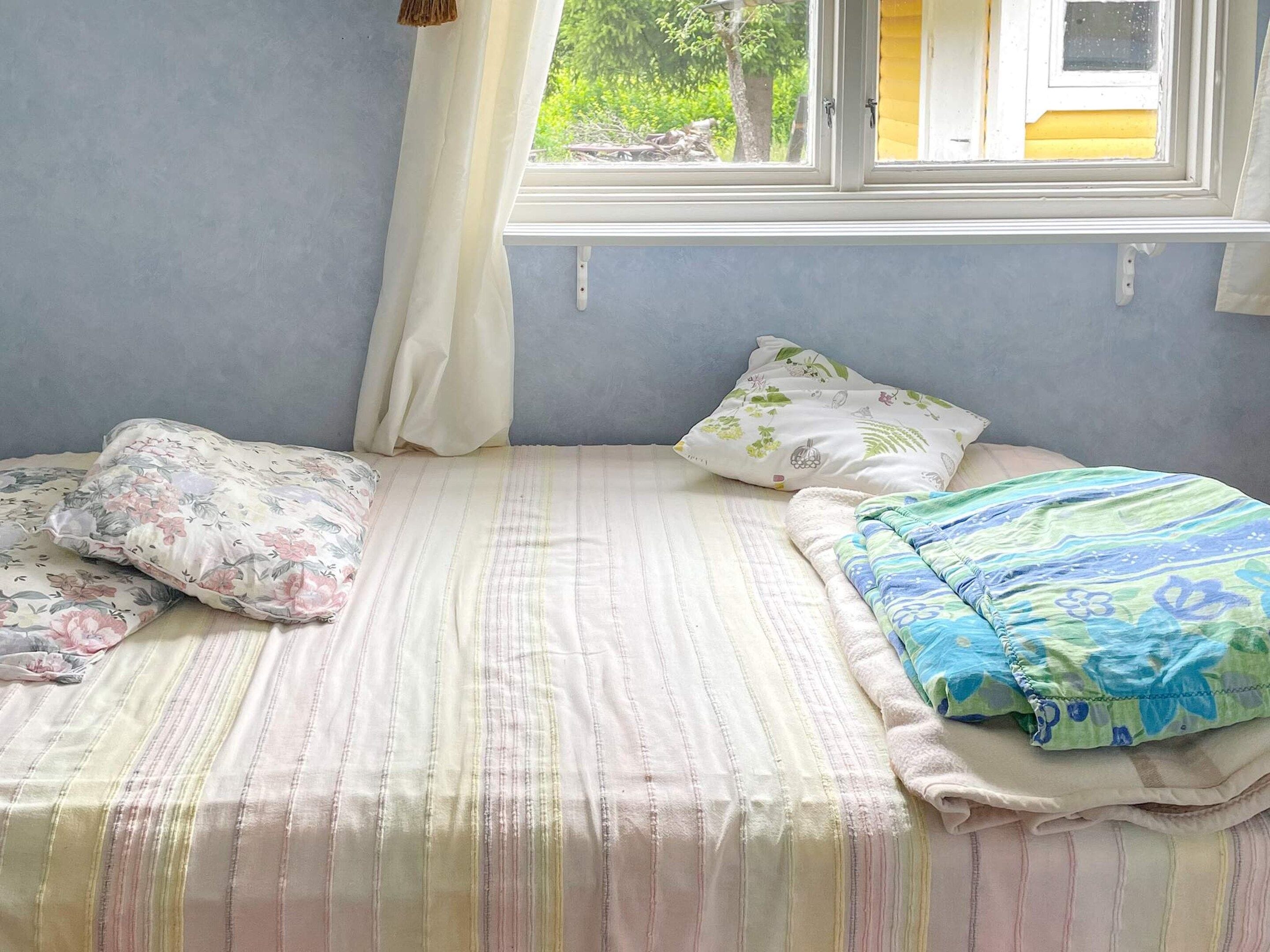 A bed with striped bedding, two pillows with floral patterns, and a blanket with a blue and green design.