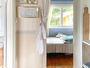 A room with a bed, a window with a view of greenery, a map on the wall, and a wooden shelf. - 4 Person Holiday Home in Kolmarden (Kolmården)