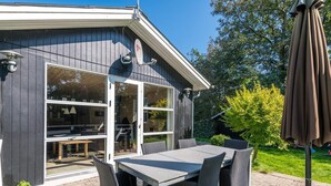 A modern house with a patio area featuring a table and chairs, a satellite dish, and a garden with a tree and grass. - 6 Person Holiday Home in Hemmet (Hemmet)