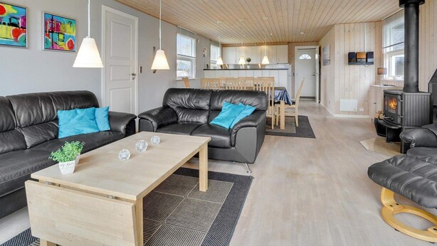 A modern living room with a fireplace, black leather sofas, a wooden coffee table, and a kitchen in the background. - 6 Person Holiday Home in Hemmet (Hemmet)