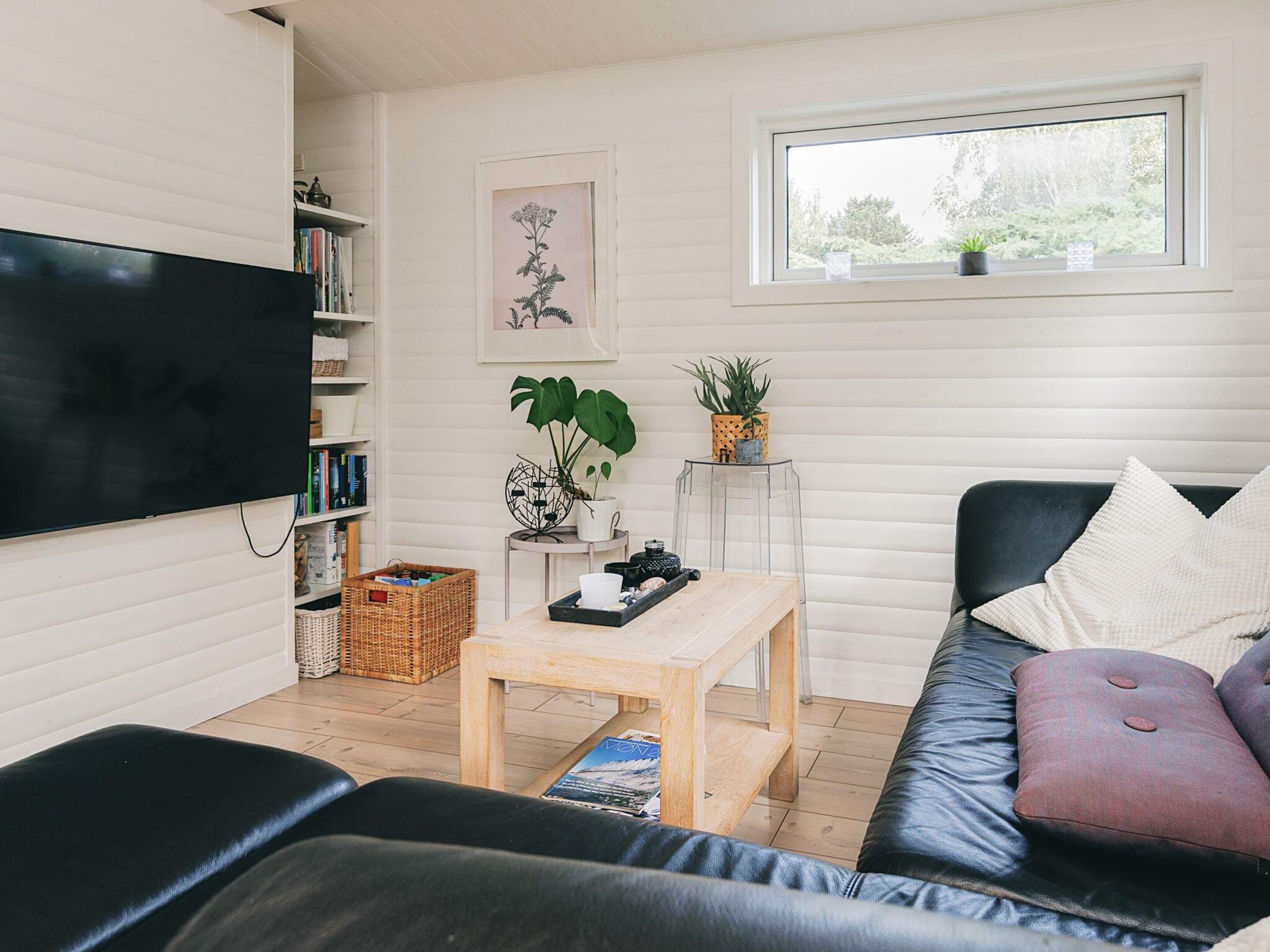 A living room with a flat-screen TV, a bookshelf, a coffee table, a sofa, and a window with a view of greenery.