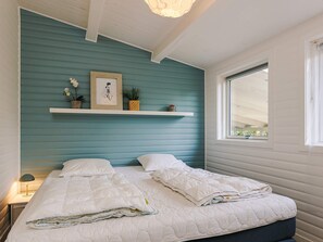 A bedroom with a bed, a nightstand, a window, and a wall-mounted shelf with decorative items. - 4 Star Holiday Home in Stege (Stege)