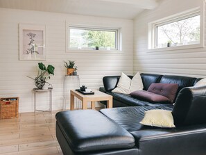 A cozy living room with a black leather sofa, a wooden coffee table, and a small side table with plants. - 4 Star Holiday Home in Stege (Stege)