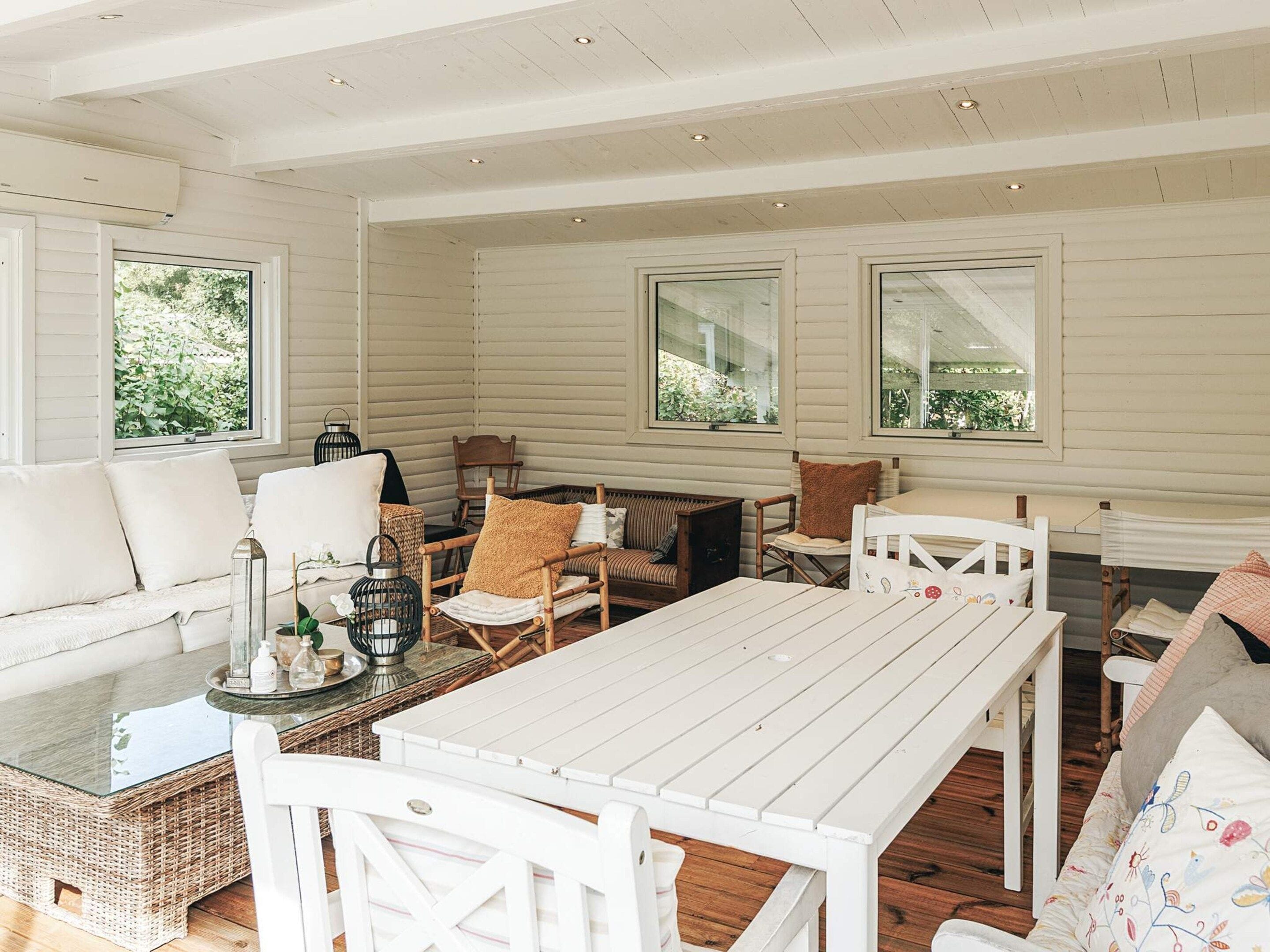 A spacious room with a white wooden table, cushioned seating, and large windows.