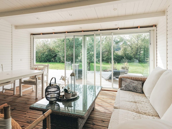 A spacious room with a large sliding glass door leading to an outdoor area, a white sofa, a glass coffee table, and a wicker side table. - 4 Star Holiday Home in Stege (Stege)