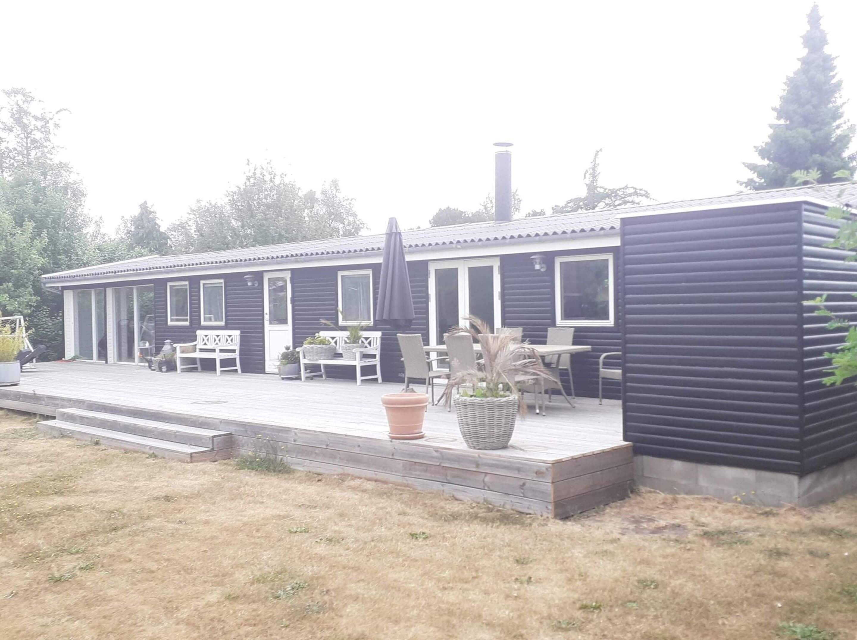 A modern house with a deck, outdoor seating, and potted plants.