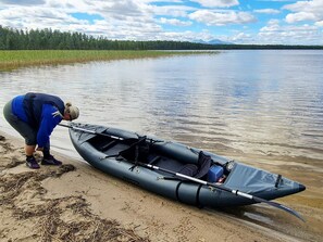 A person preparing a canoe on a calm lake with a forest in the background.