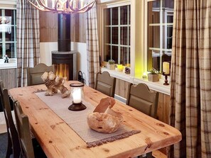 Un coin repas chaleureux avec une table en bois, une cheminée et une fenêtre agrémentée de rideaux.