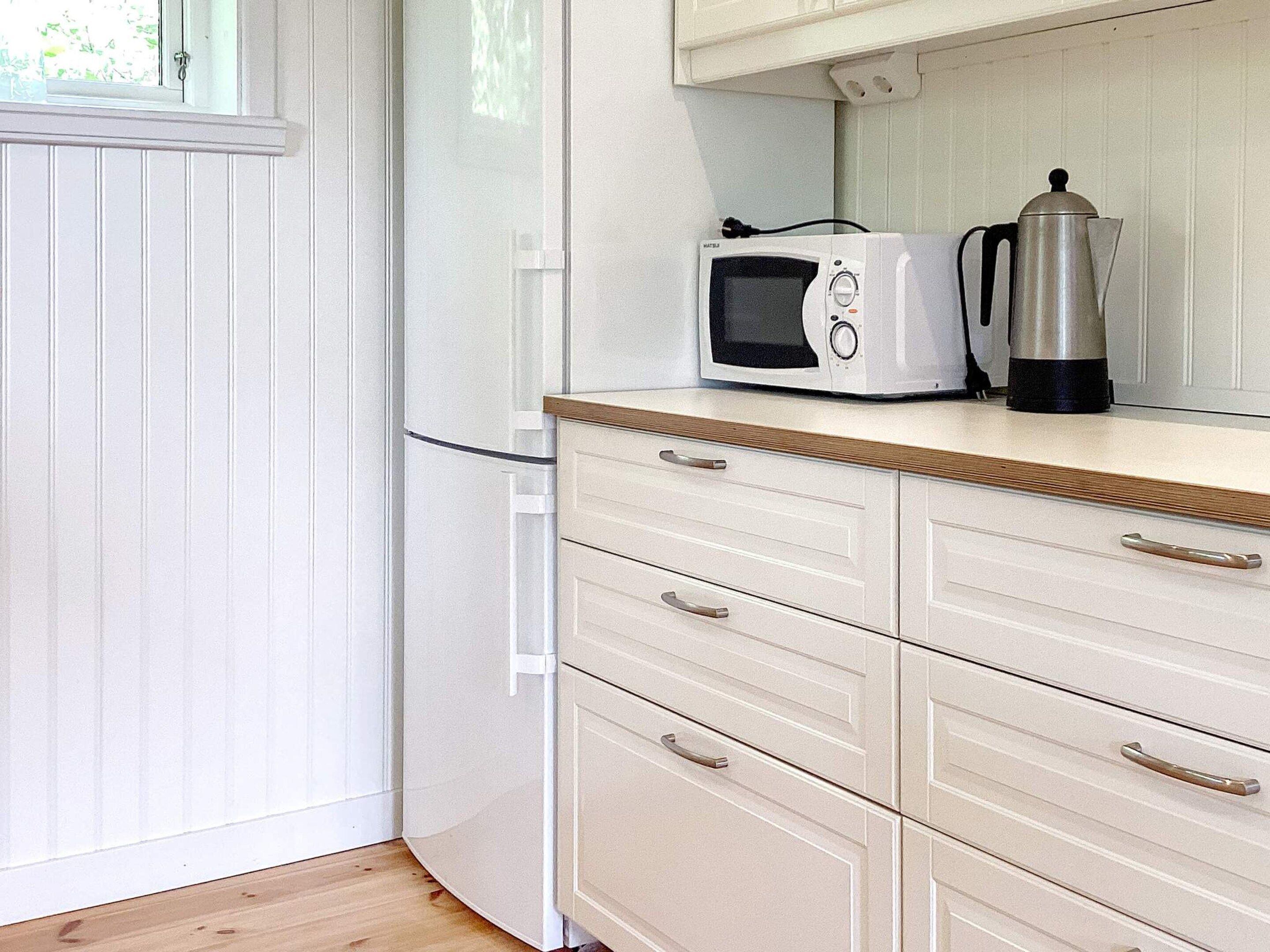 A kitchen with a microwave, a coffee pot, and a wooden countertop.