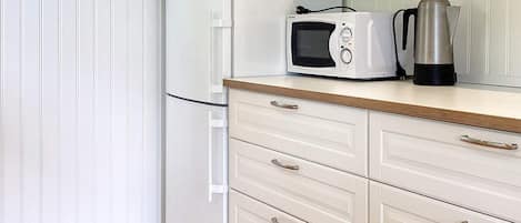 A kitchen with a microwave, a coffee pot, and a wooden countertop.