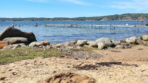 Une plage bordée d’une côte rocheuse, une jetée qui s’avance dans l’eau et des gens qui se baignent.