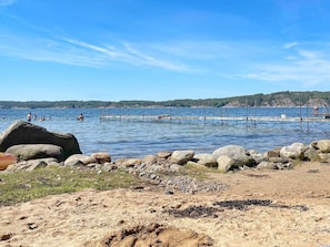 A beach with a rocky shoreline, a pier extending into the water, and people swimming. - 4 Person Holiday Home in Uddevalla (Uddevalla)
