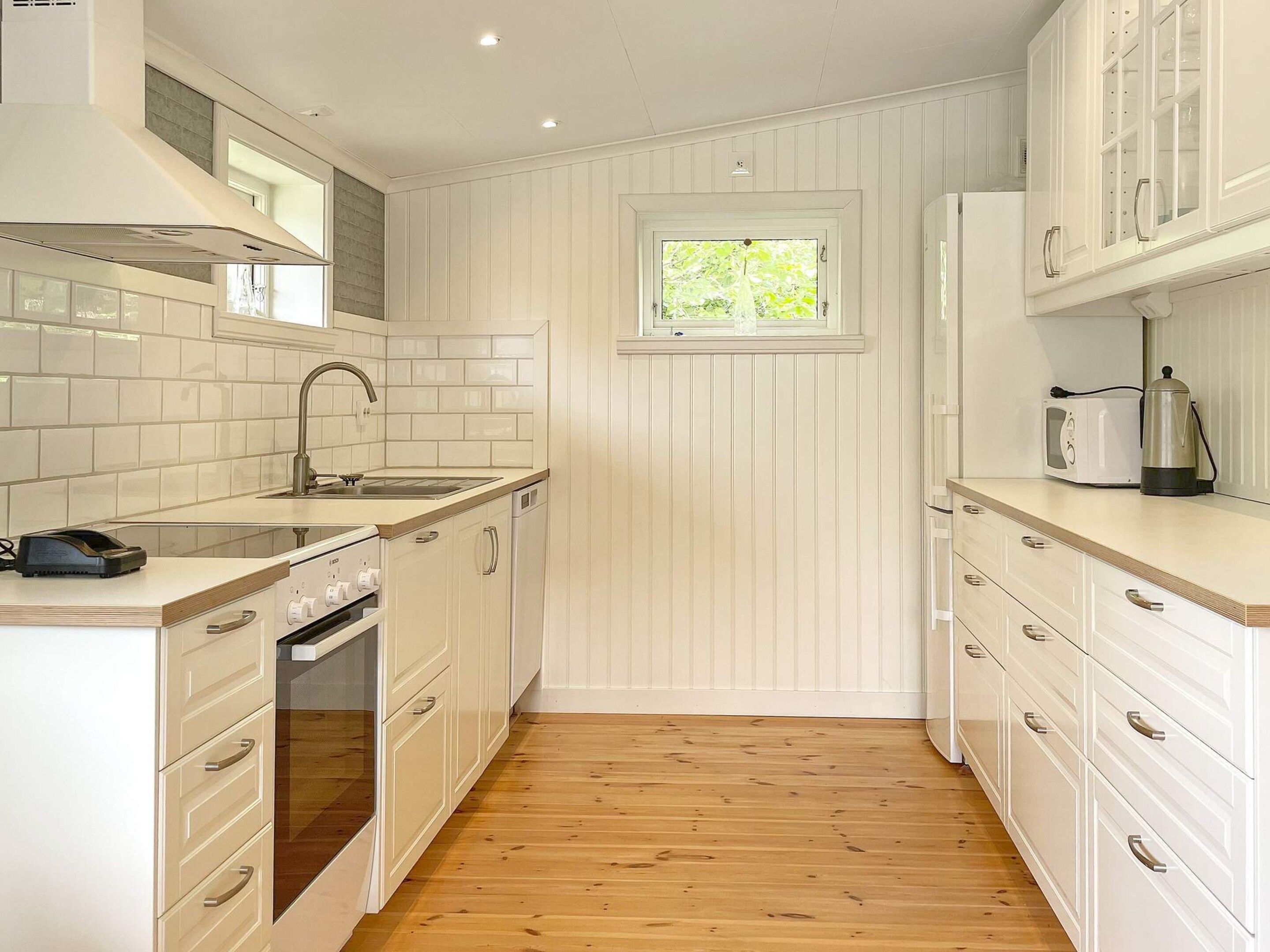 A compact kitchen with white cabinetry, a built-in oven, a sink, and a window above the countertop.