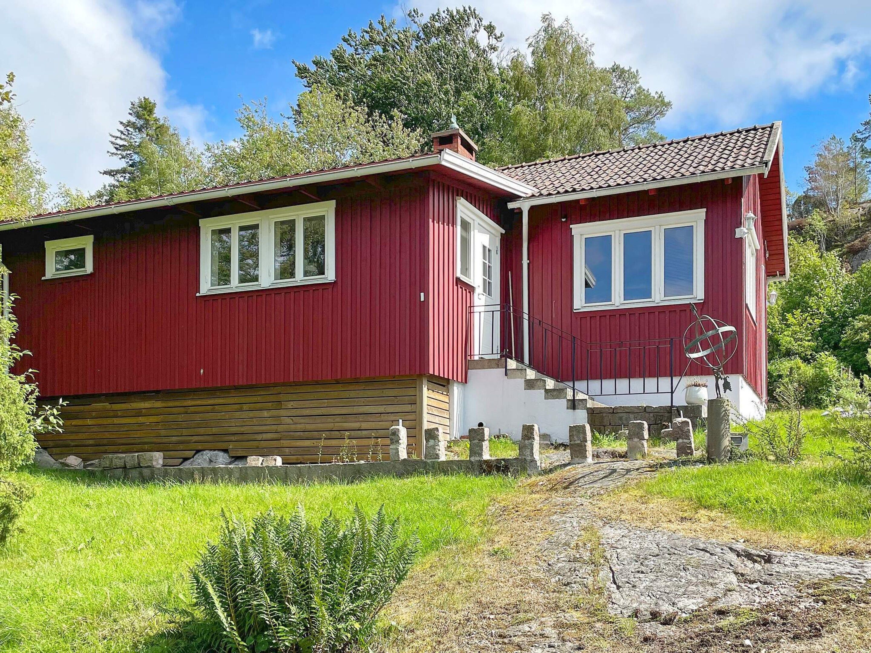 A red wooden house with a stone foundation, white trim, and a small porch.