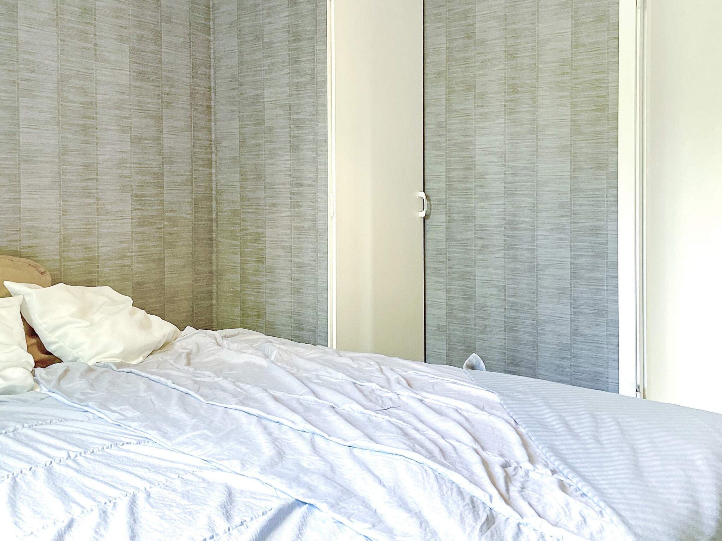 A bed with white bedding in a room with a large window and a door with a handle.