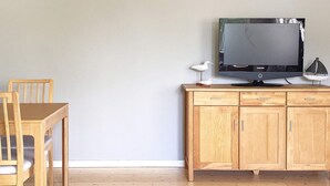 Une table à manger en bois avec des chaises, un buffet en bois avec des tiroirs, et un téléviseur à écran plat posé sur le dessus.
