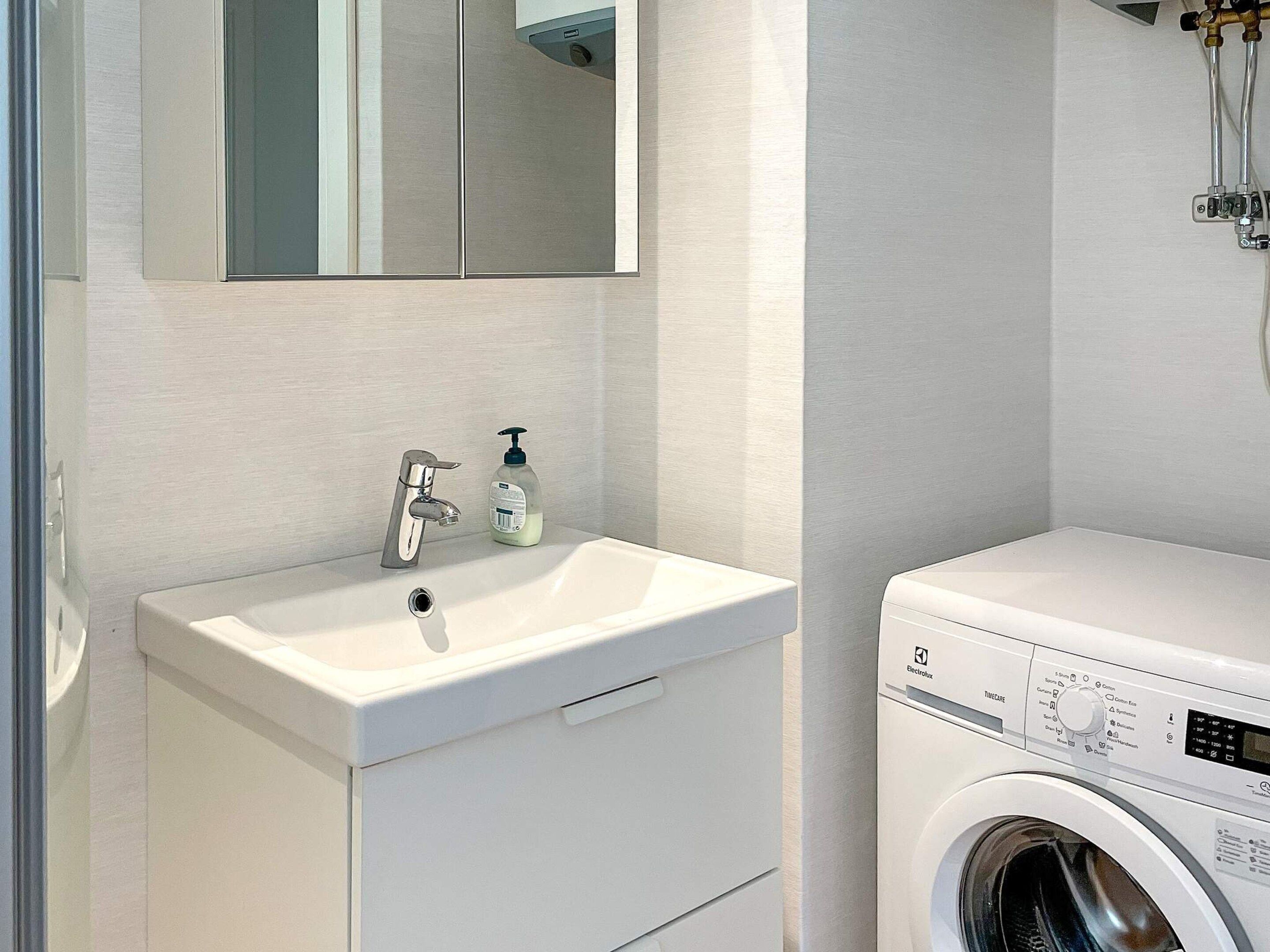 A modern bathroom with a white sink, a mirror, and a front-loading washing machine.