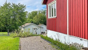 Un bâtiment rouge avec une fenêtre blanche et une porte blanche, entouré de verdure et bordé d’un chemin de gravier.