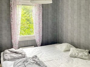 A bedroom with a bed, white bedding, a window with curtains, and a view of greenery outside. - 4 Person Holiday Home in Uddevalla (Uddevalla)