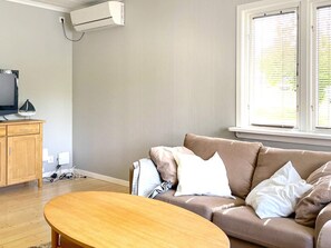 A living room with a sofa, a coffee table, a television, and an air conditioning unit. - 4 Person Holiday Home in Uddevalla (Uddevalla)