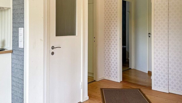 Un couloir avec une porte blanche, un mur à texture et un papier peint à motifs.