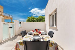An outdoor dining area with a table set for four, surrounded by chairs, with a view of a building and trees in the background. - 3878 Dalie - Appartamento by Barbarhouse (Manduria)