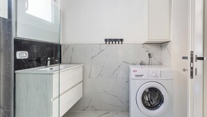Ein modernes Badezimmer mit Marmorrückwand, einer weißen Waschmaschine und einem schlichten Waschtisch.